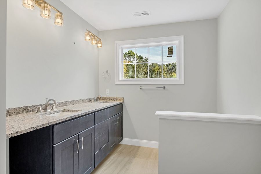 Bathroom with gray walls, dark cabinets, granite countertop, window, and light fixture.