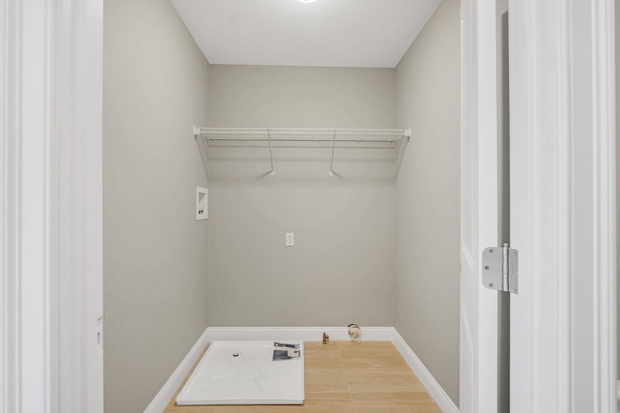 Empty laundry room with a wire shelf, light-colored walls, and wooden floor panels on the lower part.