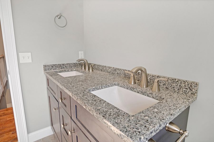 Gray double vanity with granite countertop and two sinks in a bathroom.