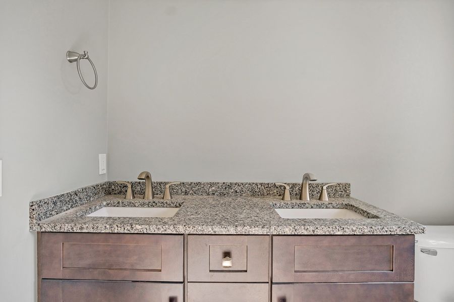 Double bathroom vanity with granite countertop, brown cabinets, and silver faucets.