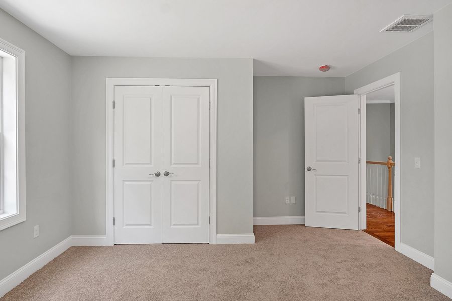 Empty bedroom with gray walls, white doors, and tan carpet. One door is open.