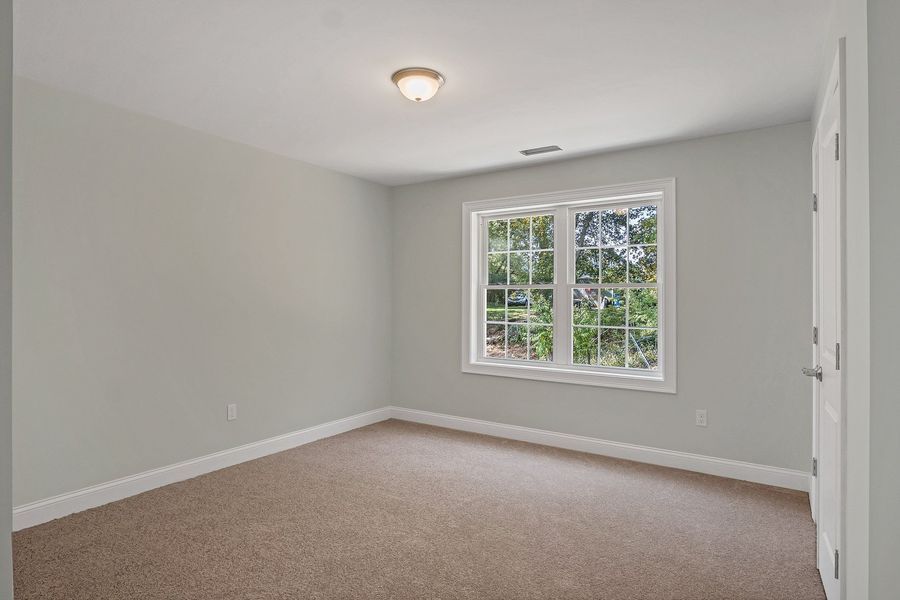 Empty room with light gray walls, brown carpet, window, and white trim.