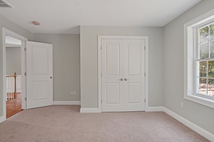 Empty bedroom with light gray walls, white trim, double doors, a door, and a window.