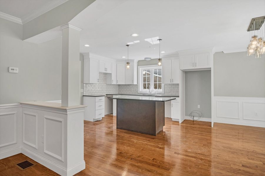 Bright, modern kitchen with white cabinets, dark island, and hardwood floors.