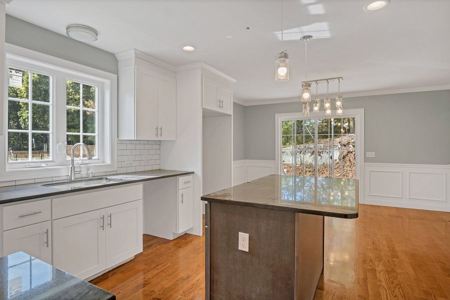 Bright kitchen with white cabinets, dark countertops, and wood floors.