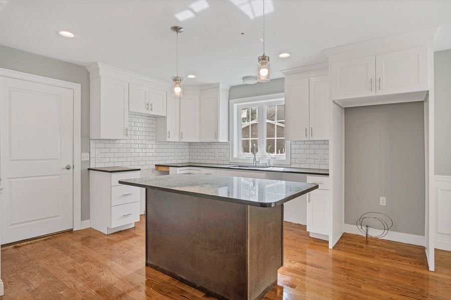 Modern kitchen with white cabinets, dark island, and hardwood floors.