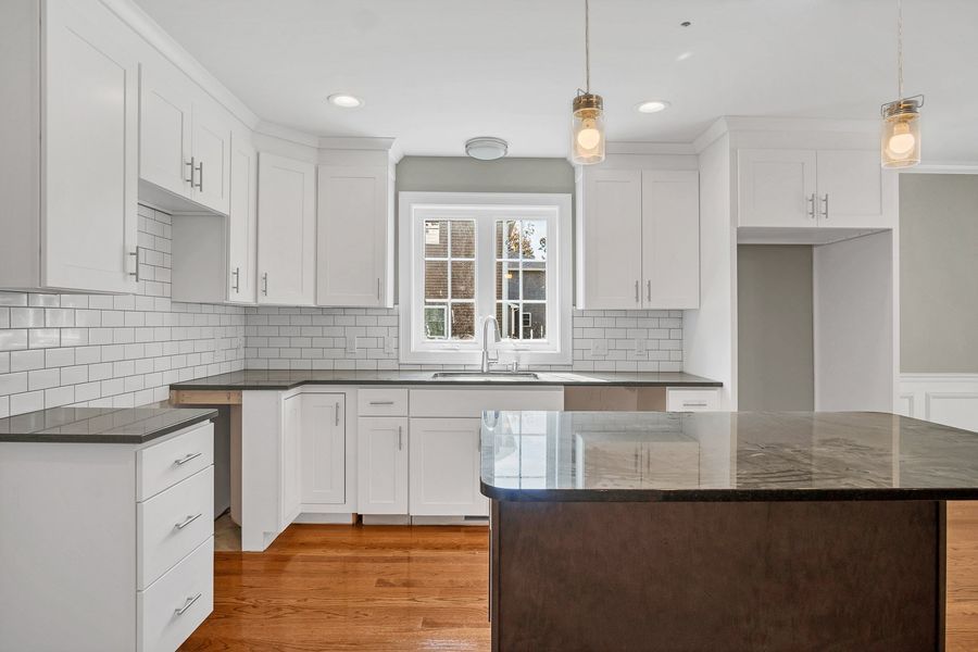 White kitchen with dark countertops, wood floors, and island.