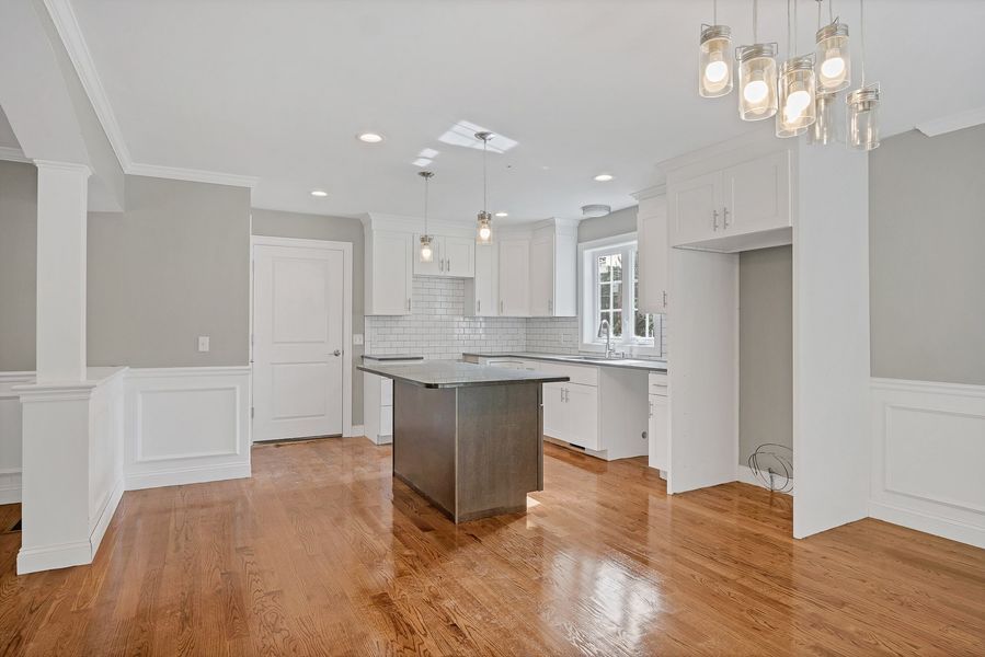 Empty modern kitchen with white cabinets, gray walls, and hardwood floors.