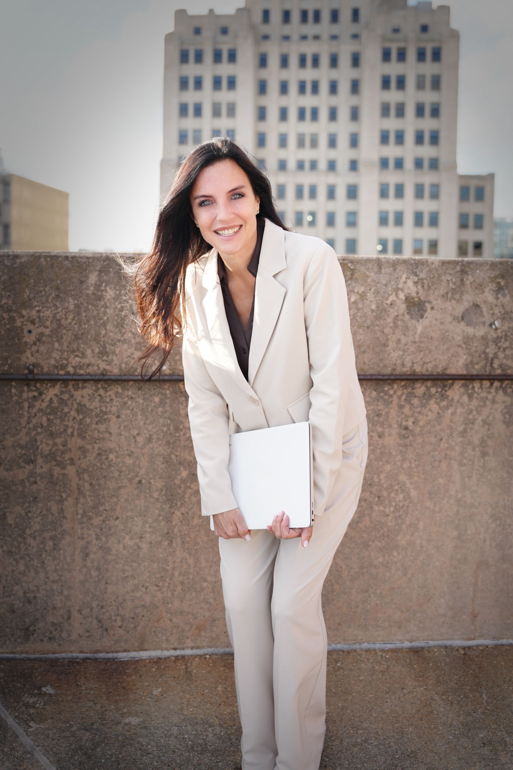 Woman leans on a ledge, gazing upwards. Buildings and a light fixture are behind her.