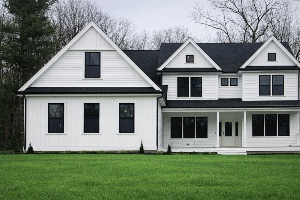 White house with black windows and roof, on green lawn under overcast sky.