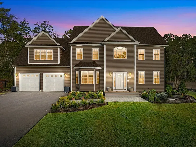 Two-story brown house with white garage doors and a front yard, surrounded by trees.