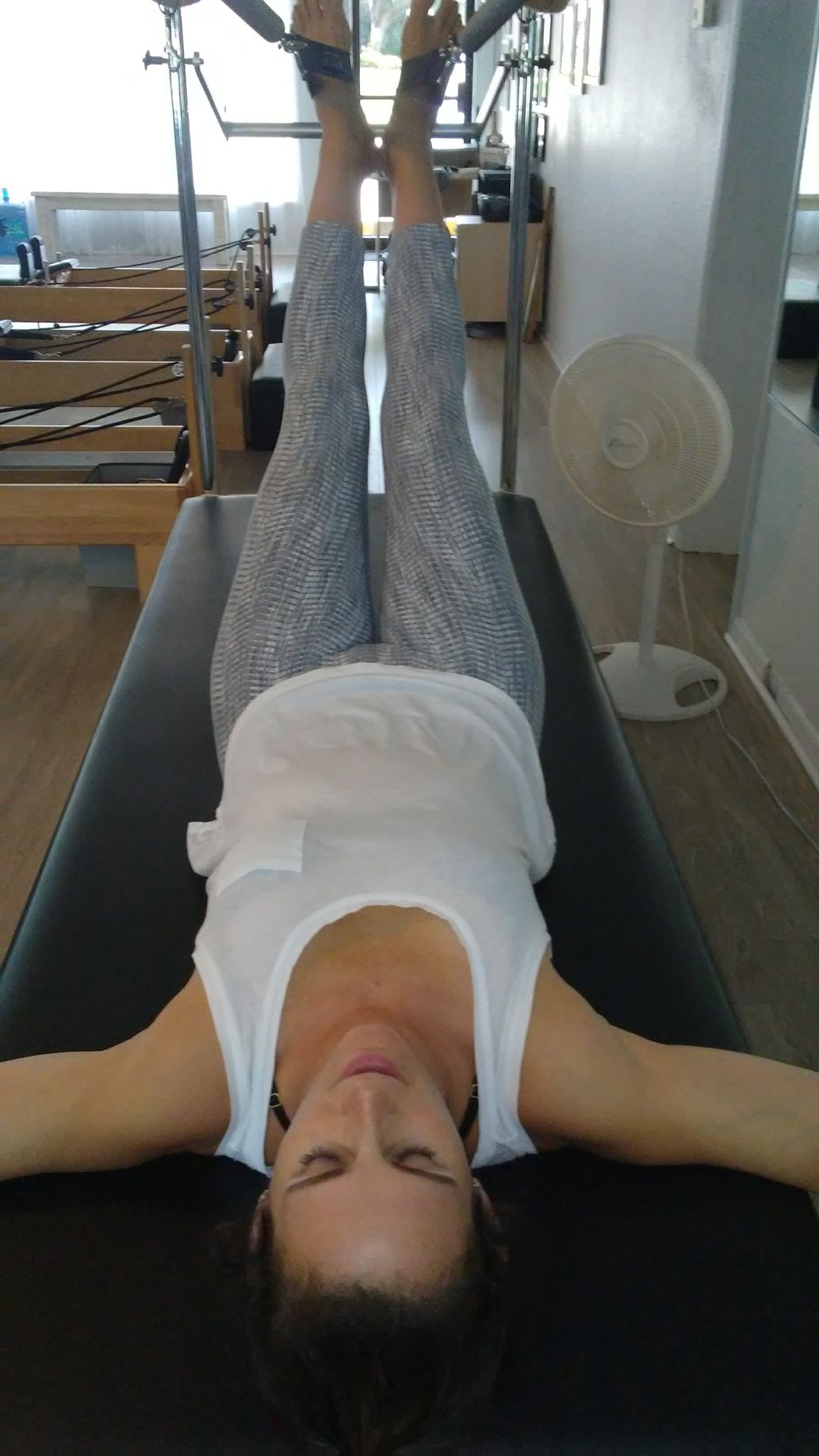 A woman is laying on a pilates mat with her legs up.