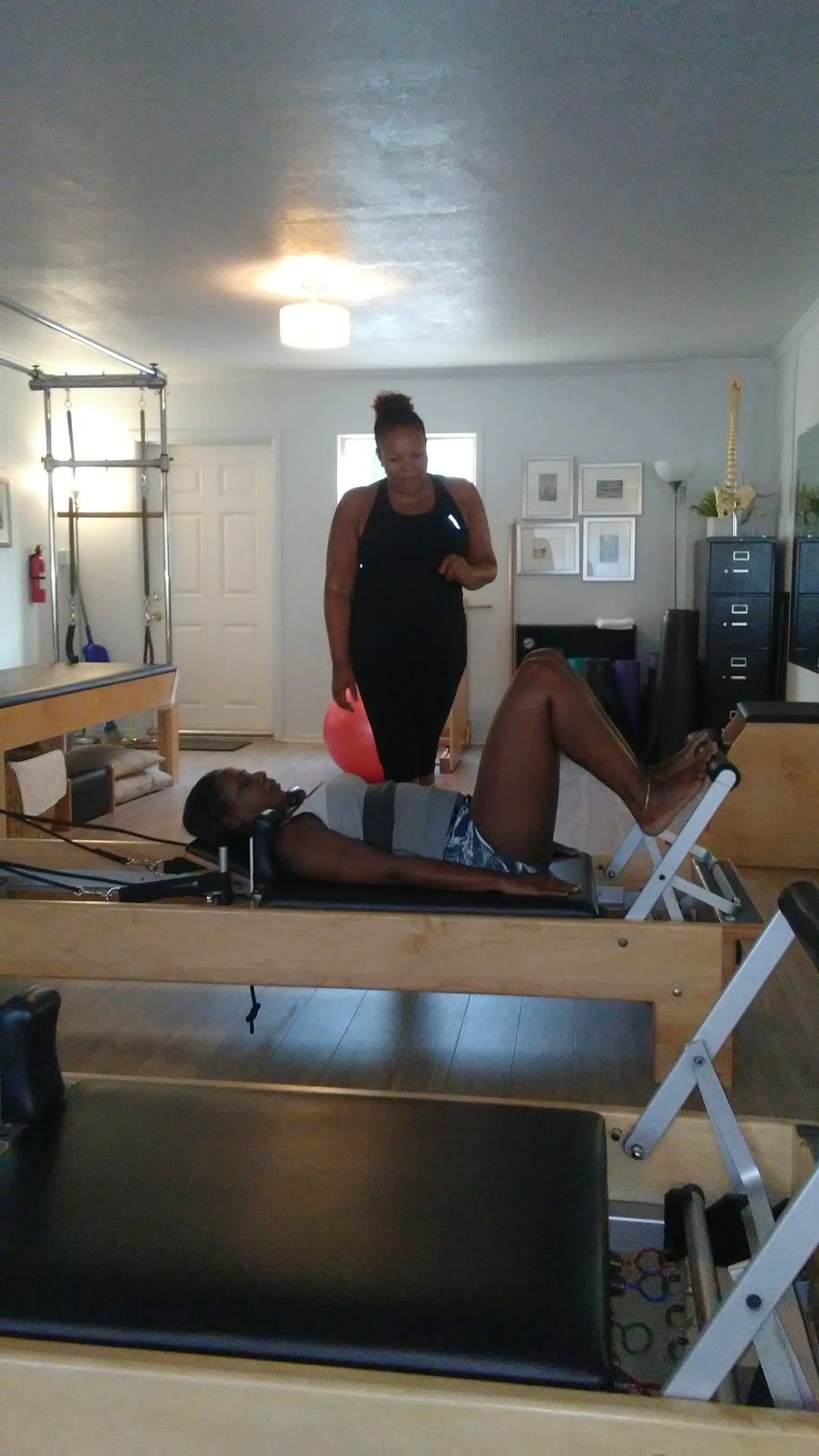 A woman is laying on a pilates machine while a woman stands behind her.