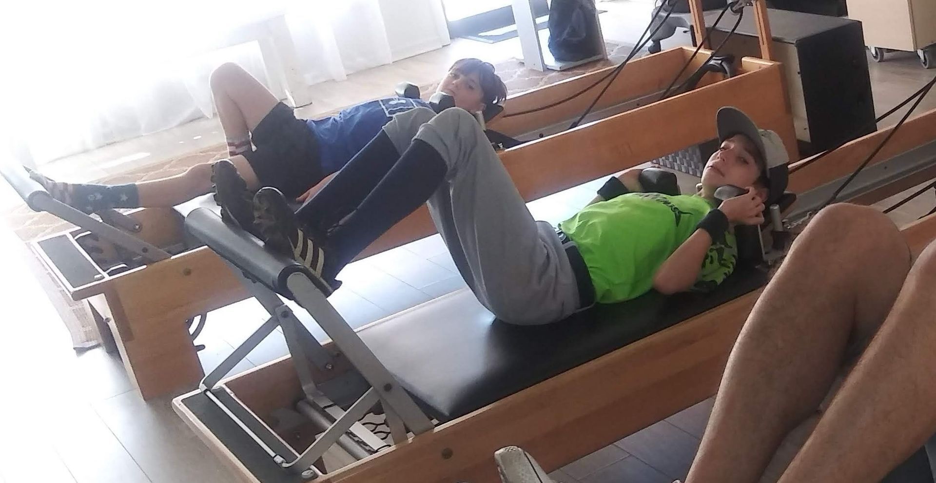 Two people are laying on pilates machines in a gym.