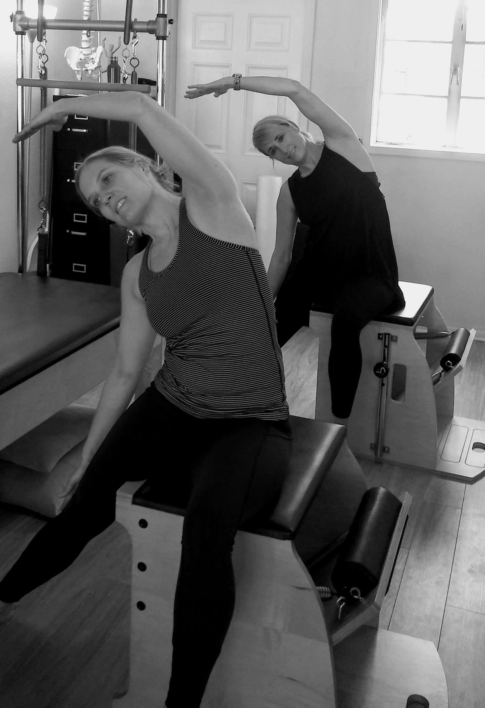 Two women are doing stretching exercises in a gym
