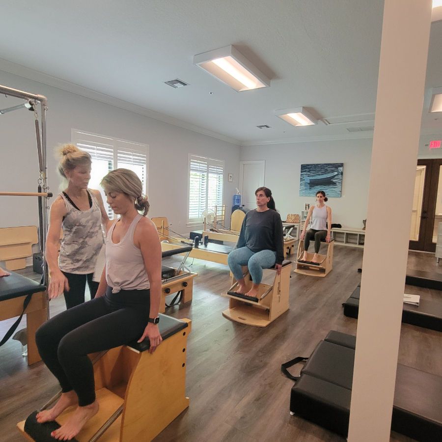 A group of women are sitting on pilates chairs in a gym.