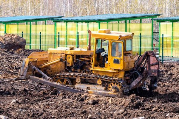A yellow bulldozer is sitting in the middle of a dirt field.