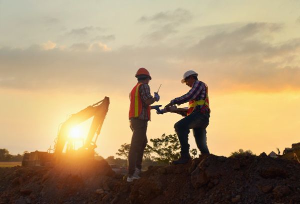 Two construction workers are working on a construction site at sunset.