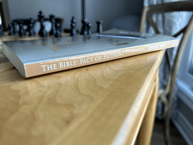 A book is sitting on top of a wooden table next to a chess board.