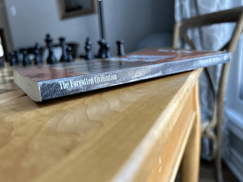 A book is sitting on a wooden table next to a chess set.
