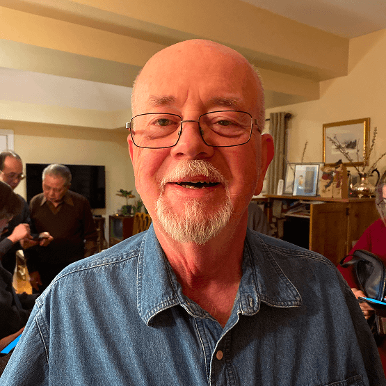 A bald man with glasses and a beard is smiling in a living room