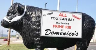 A statue of a bull with a sign that says all you can eat prime rib at domenico 's