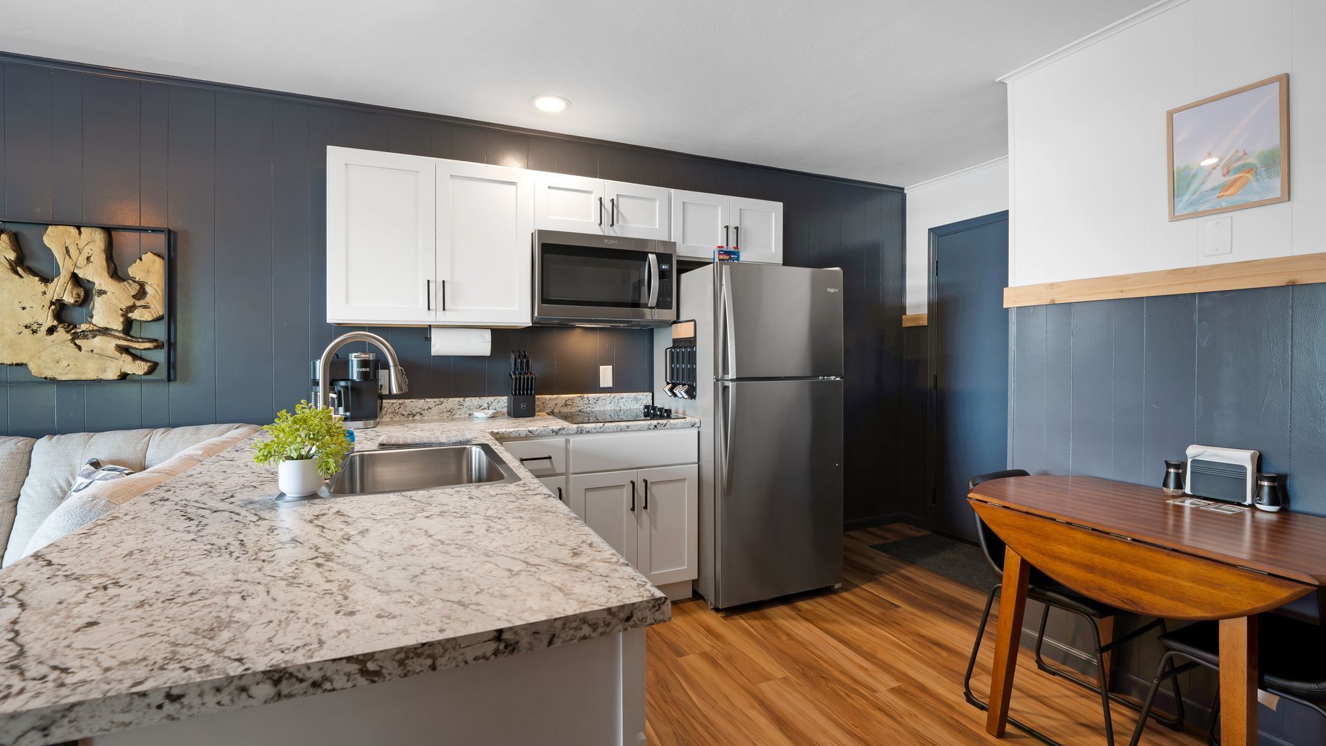 A kitchen with granite counter tops , stainless steel appliances , a refrigerator , microwave , sink and table.