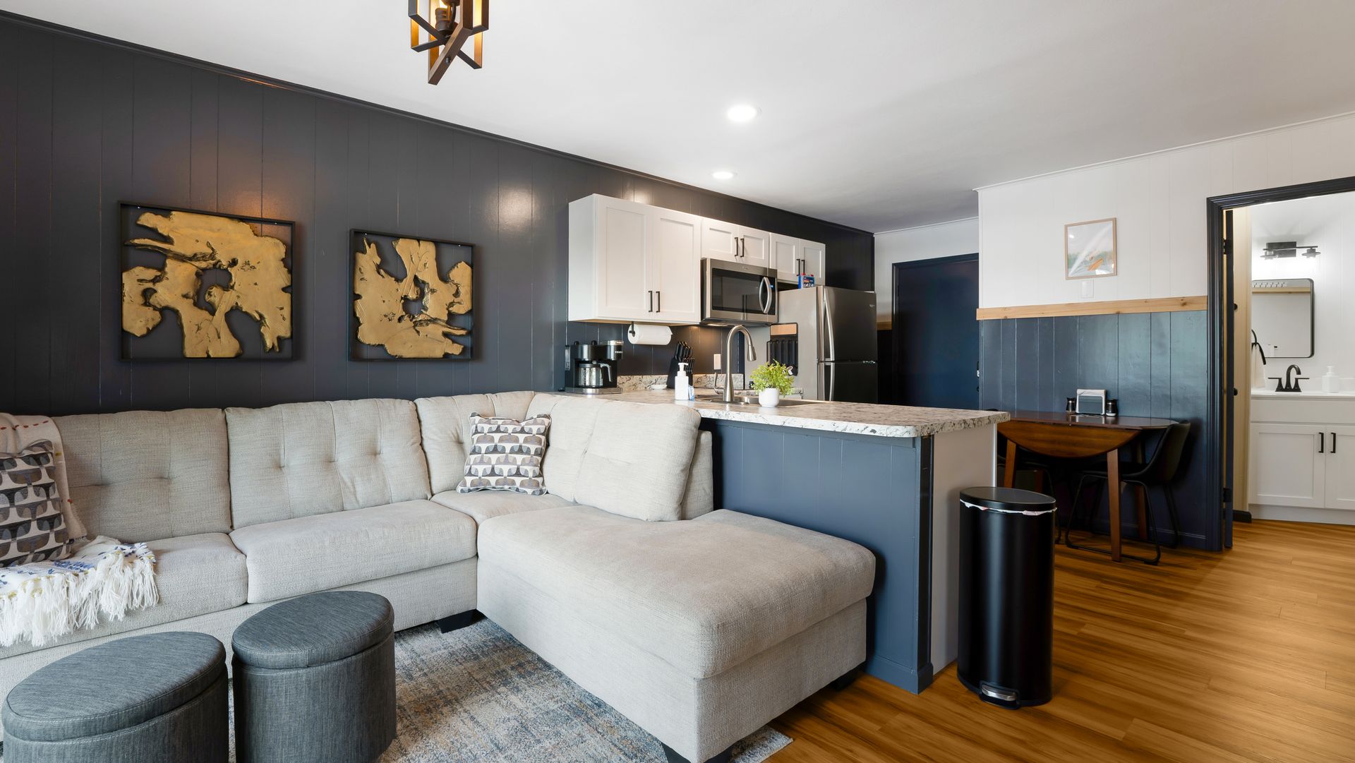 A living room with a sectional couch , ottomans , and a trash can.