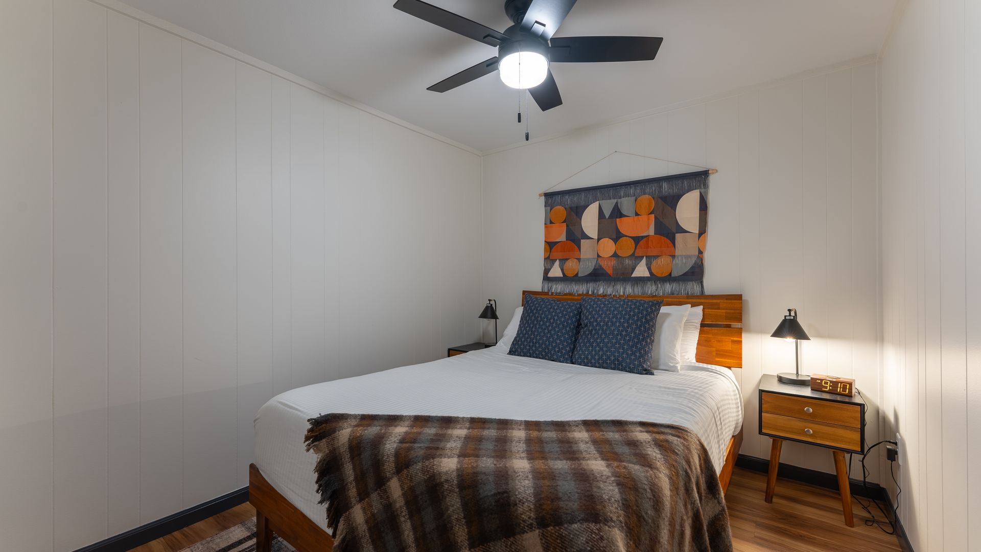 A bedroom with a bed , nightstand , lamp and ceiling fan.