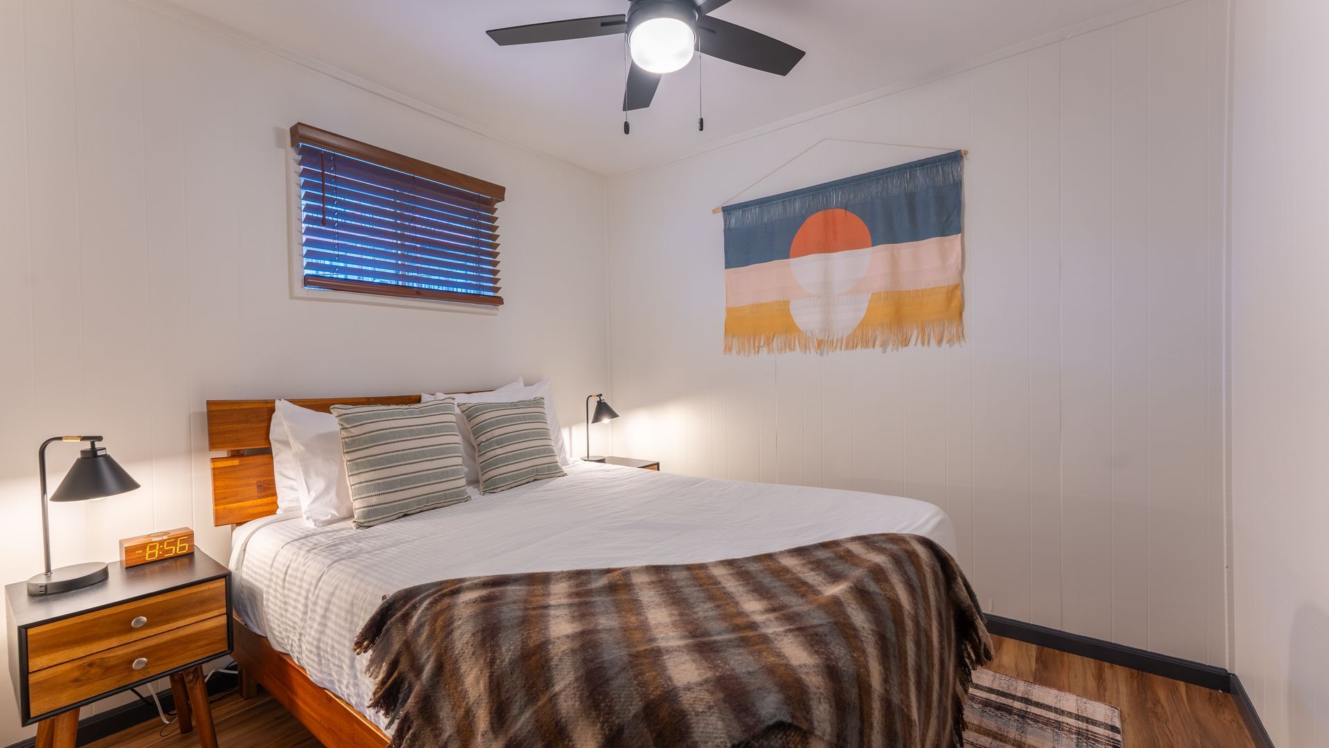 A bedroom with a bed , nightstand , lamp and ceiling fan.