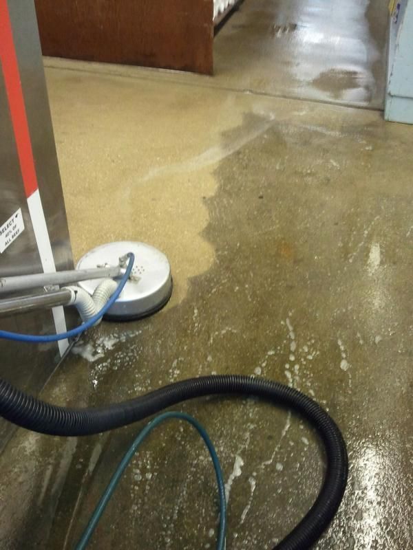 Floor being cleaned with a circular machine, leaving a wet and clean path in an industrial setting.