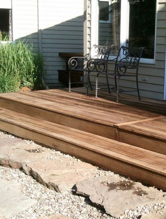 Wooden deck with stairs, two wrought iron chairs, and gravel pathway next to house.
