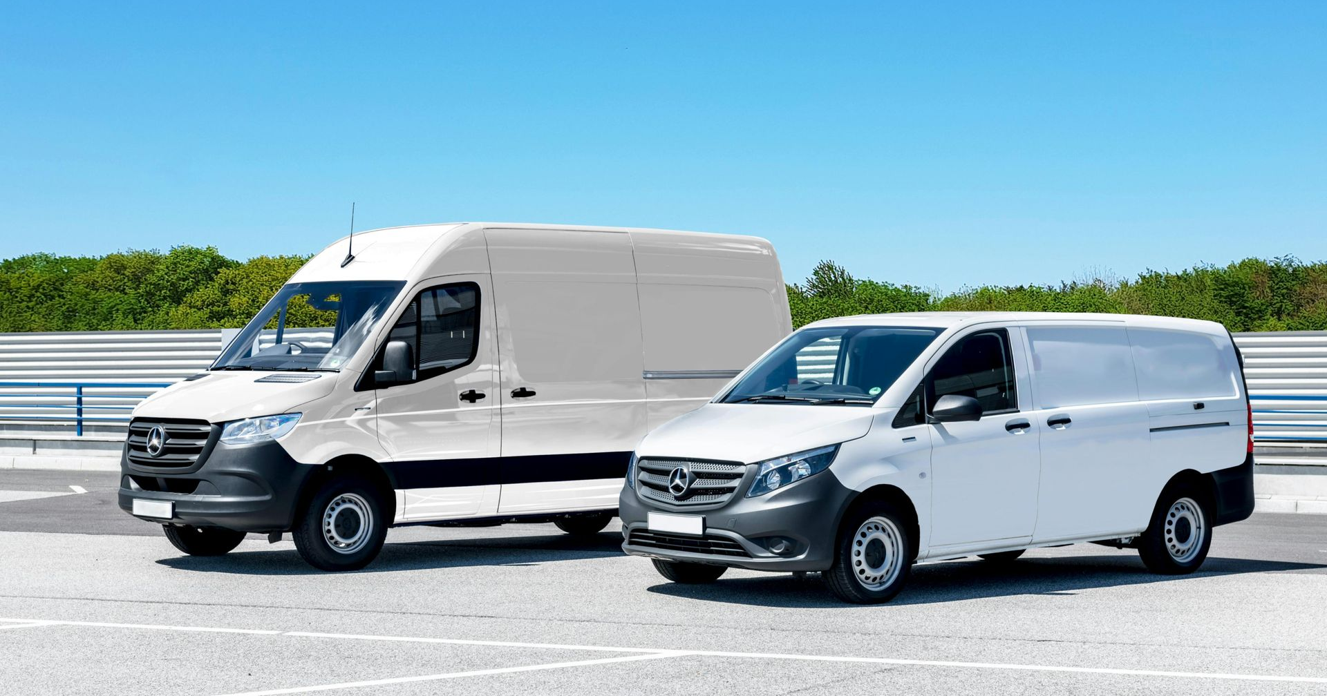 Two white Mercedes-Benz cargo vans parked side-by-side on an asphalt lot against a clear blue sky.