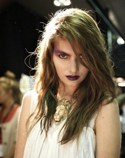 A woman with long hair and purple lipstick is wearing a lion necklace