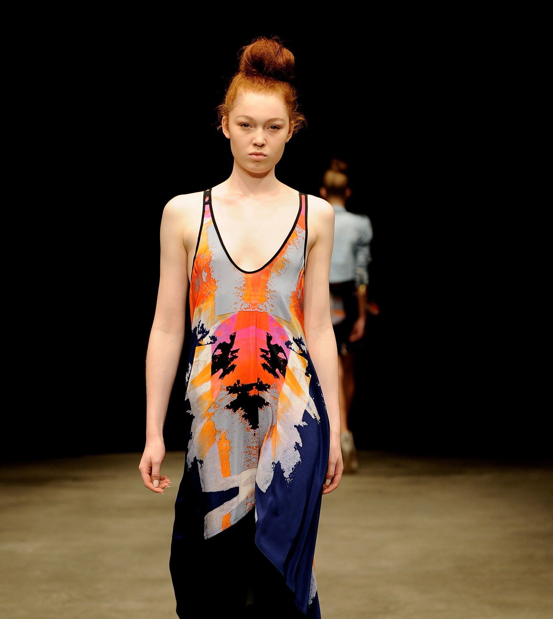 A woman is walking down a runway wearing a colorful dress