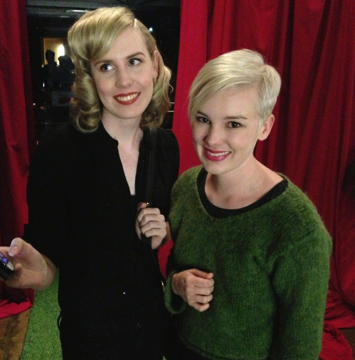 Two women standing next to each other in front of a red curtain