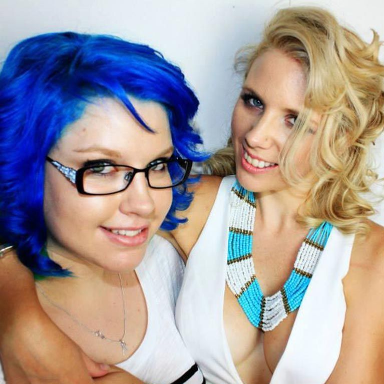 A woman with blue hair and glasses is hugging another woman