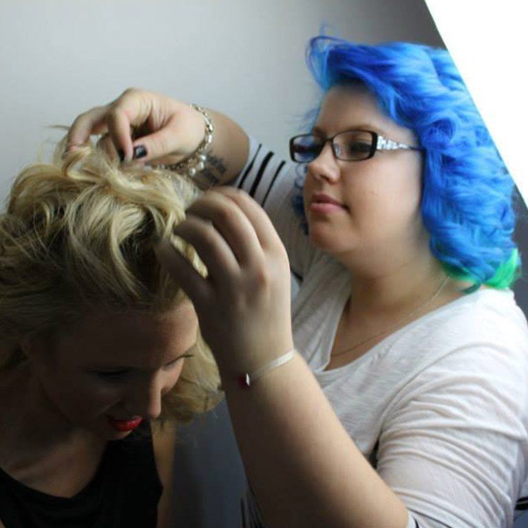 A woman with blue hair is touching another woman's hair