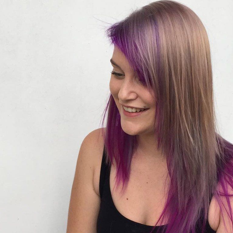 A woman with purple hair is smiling and wearing a black tank top