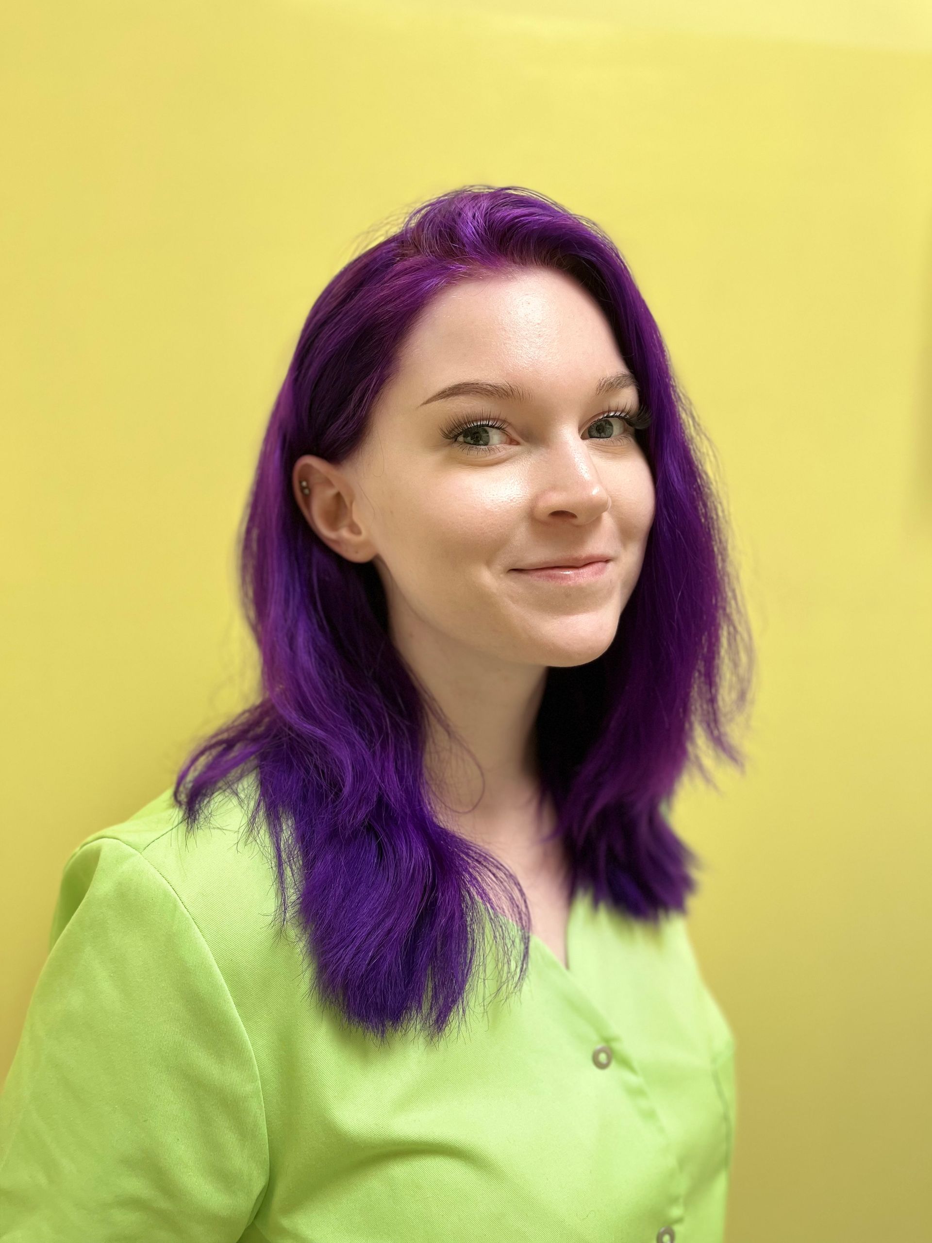 Eine Frau mit lila Haaren trägt ein grünes Hemd.