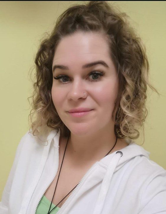 Eine Frau mit lockigem Haar trägt einen weißen Kapuzenpullover und ein grünes Tanktop.