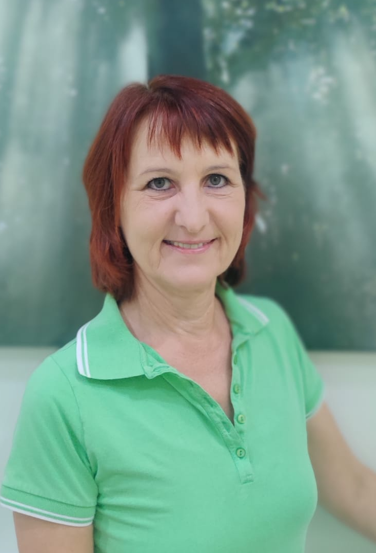 Eine Frau mit roten Haaren trägt ein grünes Poloshirt und lächelt.