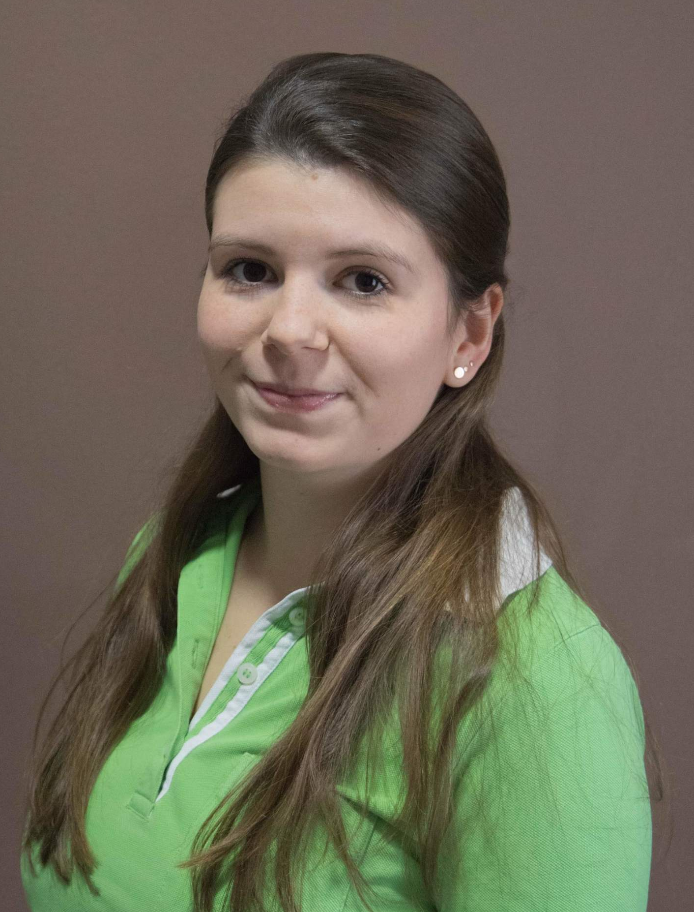 Eine Frau in einem grünen Hemd und mit Ohrringen lächelt in die Kamera.