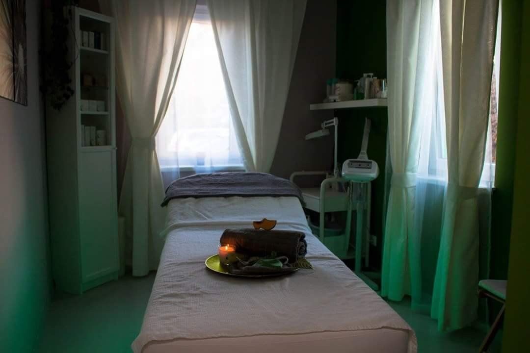 Ein Massagetisch in einem Raum mit grünen Vorhängen und einem Fenster.