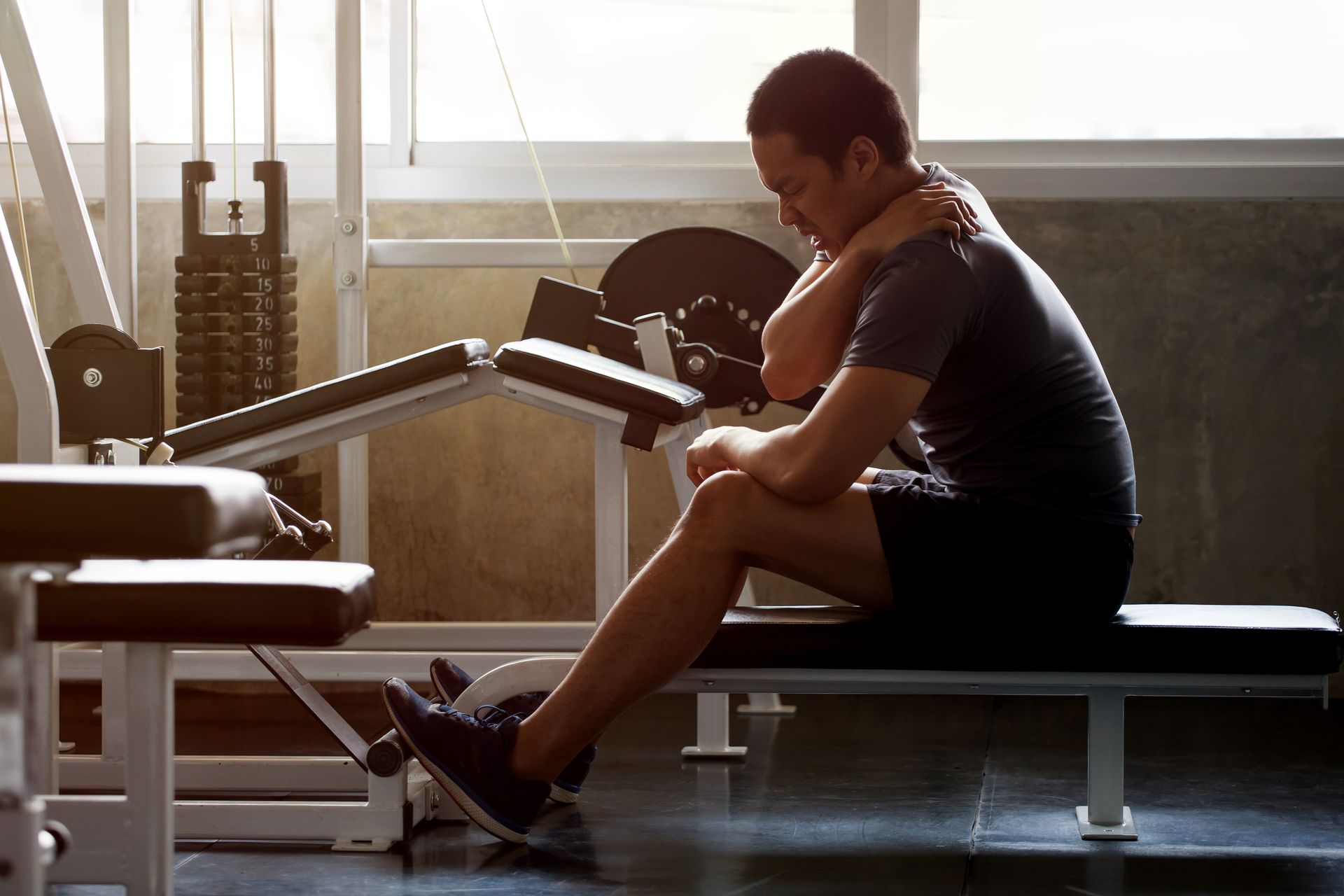 A man is sitting on a bench in a gym with his head down.