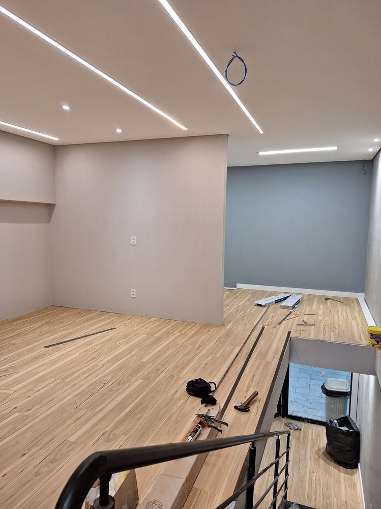 Renovation in progress in a modern room with unfinished wood flooring, exposed wiring, and recessed ceiling lights