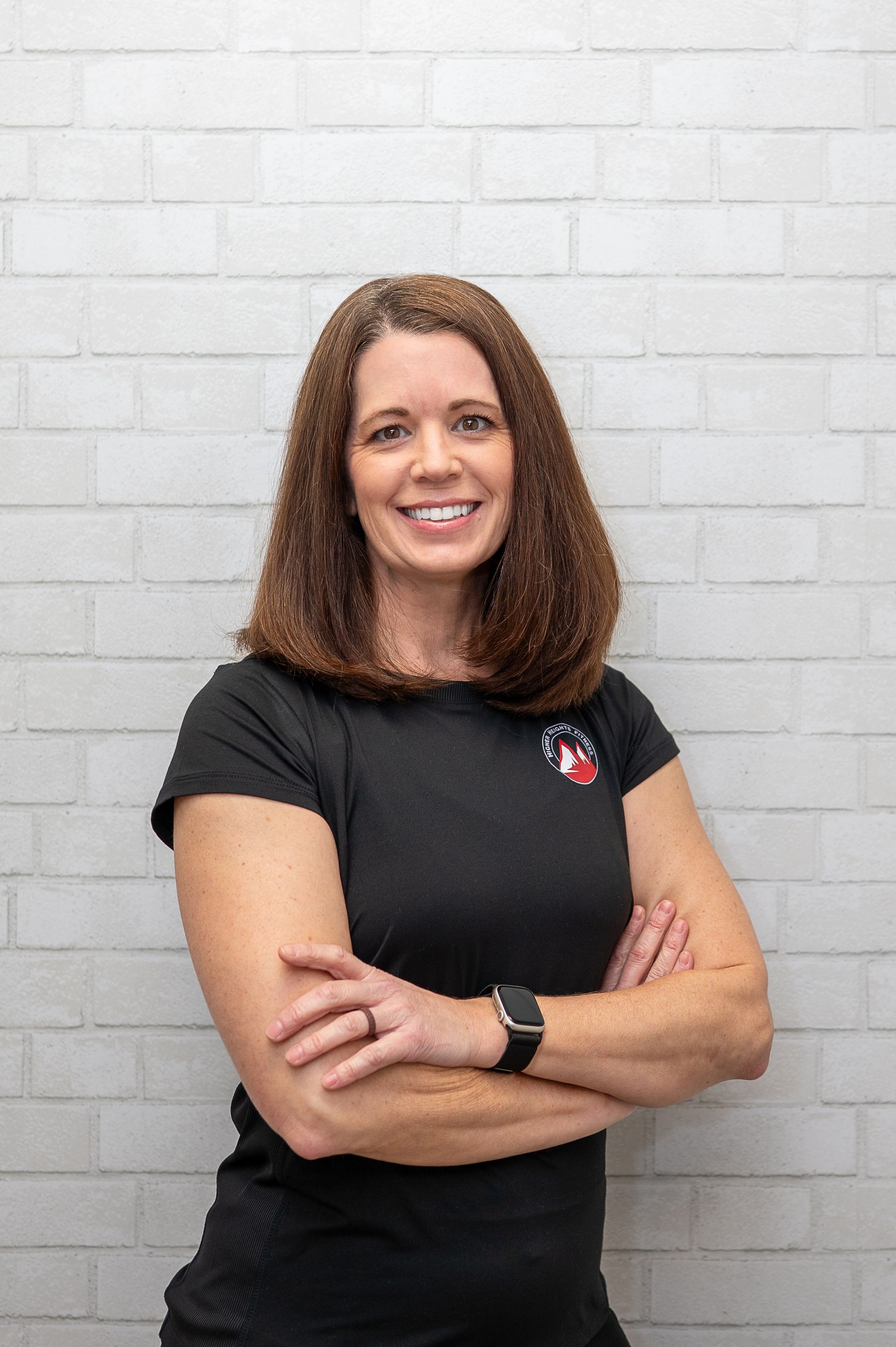 Woman with arms crossed, smiling, in front of a blue phoenix logo and business name on a wall.