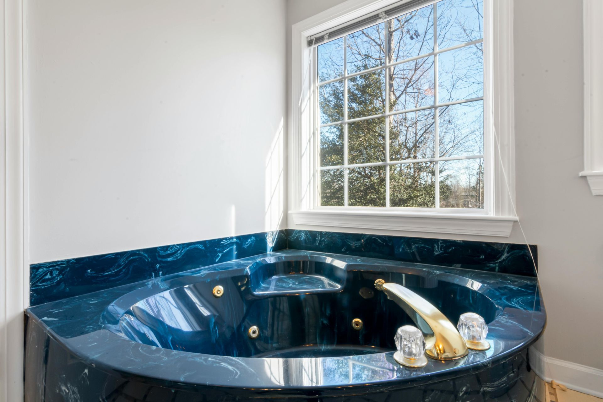 Dark blue marble whirlpool tub in a bathroom, next to a window with a view of trees.