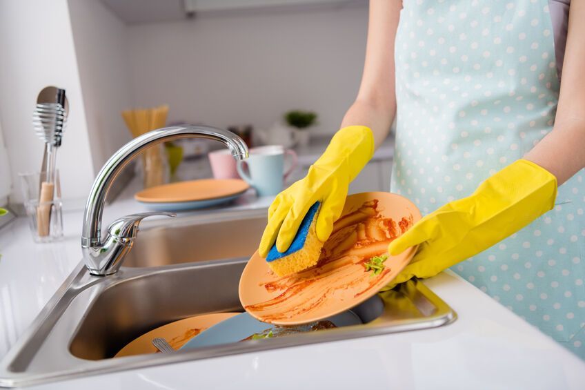 A woman wearing yellow gloves is washing dishes in a kitchen sink.