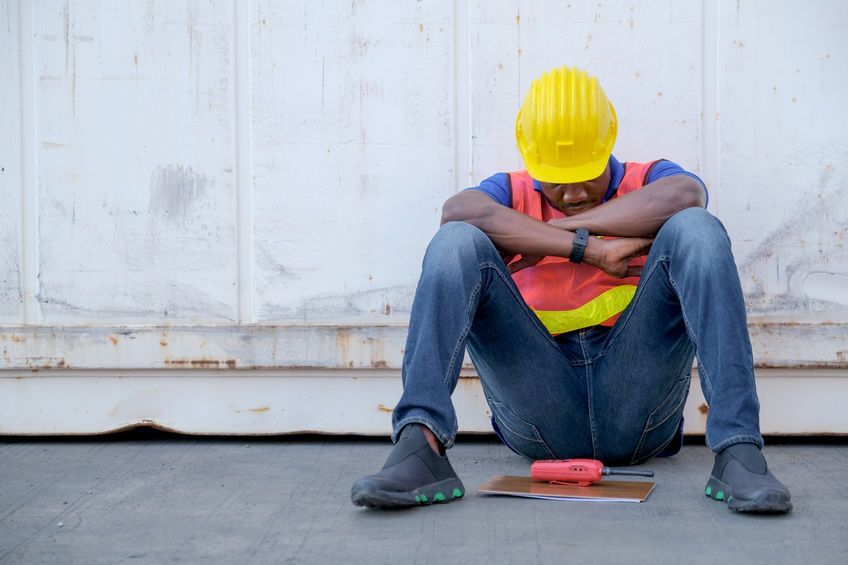 A construction worker is sitting on the ground with his head down.